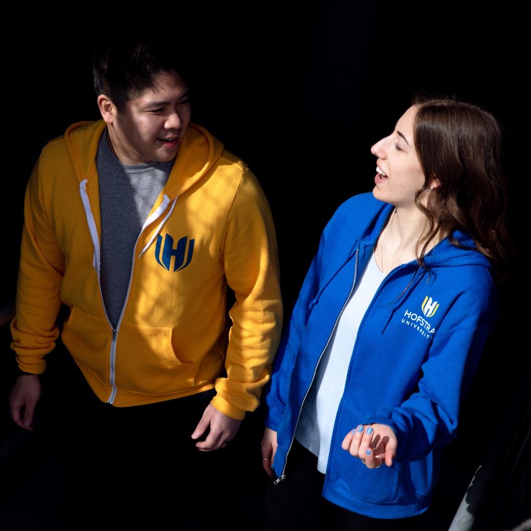 Hofstra University students wearing official blue and yellow hoodies with university logo, walking together and talking
